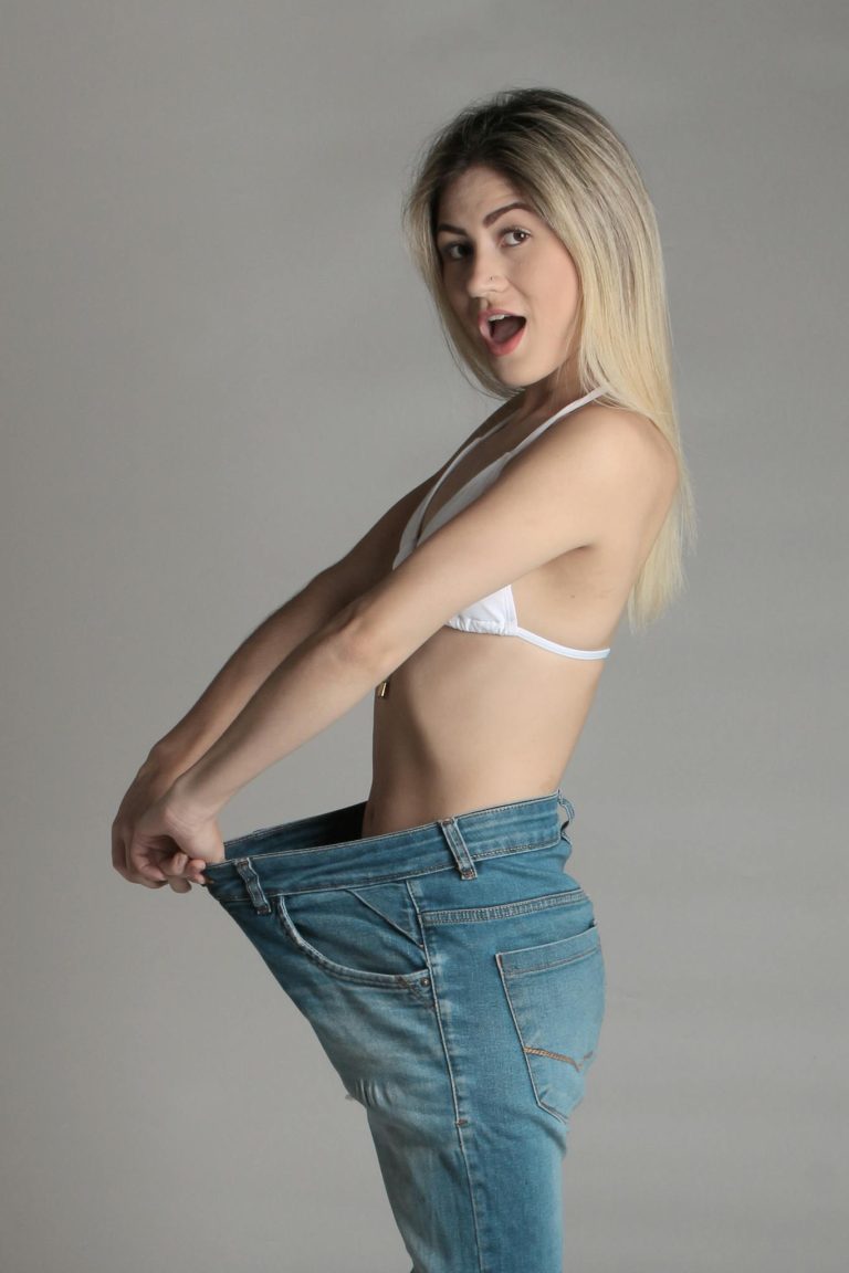 A happy woman shows off her weight loss success in studio setting.