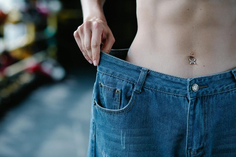 Close-up view of a slim waist and loose jeans representing weight loss or fitness progress.
